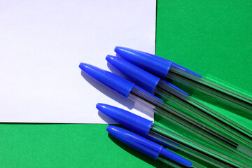 Ballpoint pens for writing on green background. View from above. The case handles white, caps blue. Handles are located in the bottom right corner. Education. Schooling. For work. Flatlay. Copy spase.