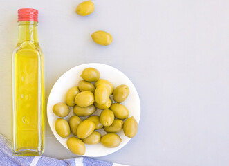 A glass bottle of olive oil, a bowl of olives, and a towel. Grey background, space for text.