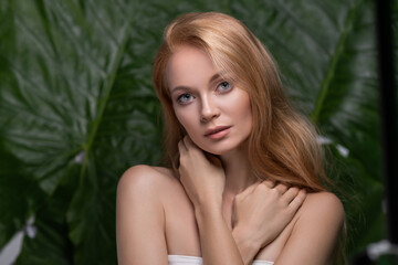 Fototapeta premium Beauty portrait of sensual ginger woman with long hair posing with green leaf over green tropical background