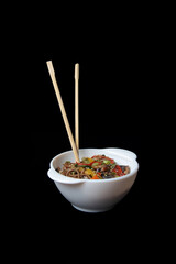 a bowl of wok noodles and chopsticks isolated on black background. Vertical image