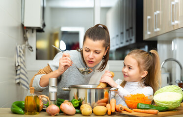 Positive young mother and little daughter tasting vegetable soup together