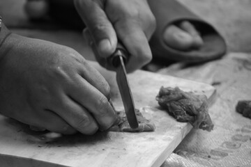 close up, black and white photo. someone was cutting meat using a knife on a wooden board.