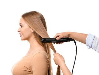 Hairdresser straightening hair of beautiful young woman against white background