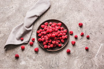 Plate with ripe raspberries on grey background