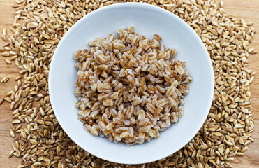 Boiled spelt in a bowl isolated on wooden background with seeds