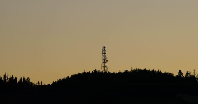 View of the tops of the hill where the radio tower is dark trees hidden in the background of shadows and silhouettes of clouds moving on the horizon during sunset.