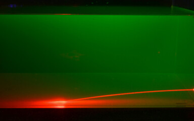 A red laser beam shines trough a green flourescent liquid. The beam is deflected due to an irregular distribution of sugar in the liquid.