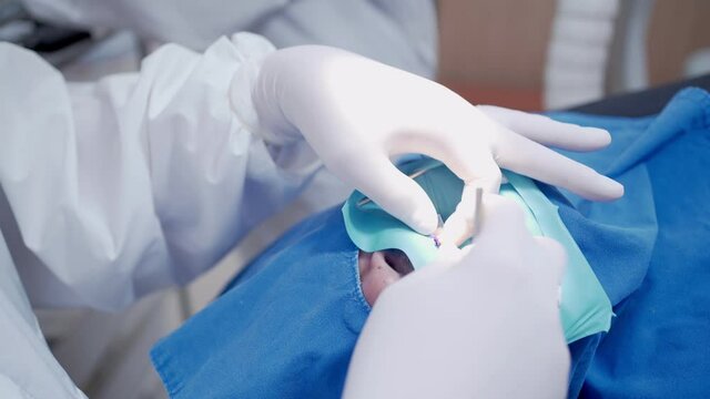 Dentist and nurse inside operating room working on oral case, patient lying down face covered, Ppe suit protective mask face shield and white protective gloves, covid-19 corona virus protection
