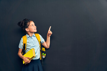 smart girl in uniform with backpack and book in her hand, pointing up
