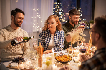 holidays and celebration concept - happy friends having christmas dinner at home pouring red wine