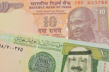 A macro image of a orange ten rupee bill from India paired up with a green and yellow one riyal...