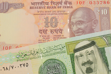 A macro image of a orange ten rupee bill from India paired up with a green and yellow one riyal bank note from Saudi Arabia.  Shot close up in macro.
