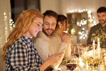holidays and celebration concept - happy friends with smartphone having christmas dinner party at home