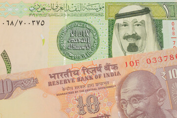 A macro image of a orange ten rupee bill from India paired up with a green and yellow one riyal...