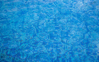Background reflection of the sun on blue transparent water ripples of the pool with a mosaic bottom.Space for text