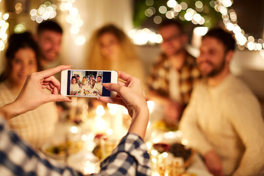 holidays, celebration and people concept - happy friends taking picture with smartphone at home christmas dinner party