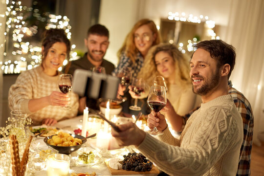holidays, celebration and people concept - happy friends drinking non-alcoholic red wine and taking picture with smartphone on selfie stick at home christmas dinner party