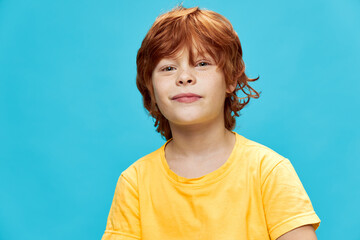 Happy boy with red hair in a yellow t-shirt on a blue background 