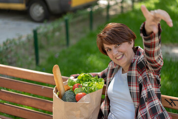 Carrying a healthy bag. Beautiful middle age woman holding paper shopping bag full of fresh vegetables and smiling. Showing that she is happy.