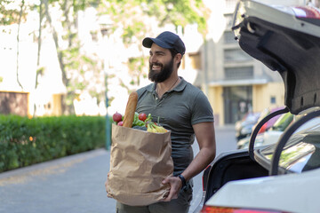Young man with strong beard carrying  fresh groceries that he bought in super market.