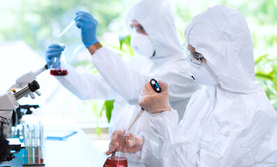 Scientists in protection suits and masks working in research lab using laboratory equipment:...