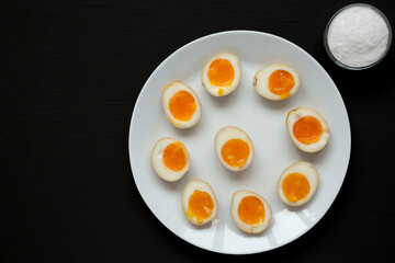Homemade Unami Soy Sauce Eggs on a white plate on a black surface, top view. Overhead, from above, flat lay. Copy space.