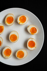 Homemade Unami Soy Sauce Eggs on a white plate on a black surface, top view. Overhead, from above, flat lay.