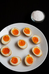 Homemade Unami Soy Sauce Eggs on a white plate on a black background, side view.