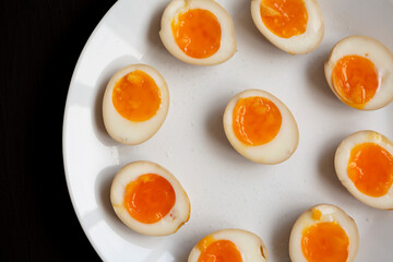 Homemade Unami Soy Sauce Eggs on a white plate on a black background, top view. Close-up.