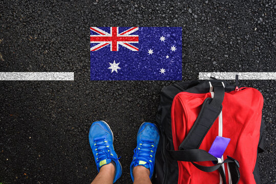 a man with a shoes and travel bag is standing on asphalt next to flag of Australia  and border