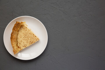 Piece of Homemade Sugar Cream Pie on a white plate on a gray surface, top view. Flat lay, overhead, from above. Space for text.
