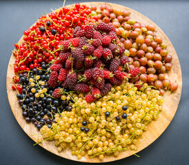 Picking summer berries on a wooden plate - black, yellow and red currants, raspberries and gooseberries