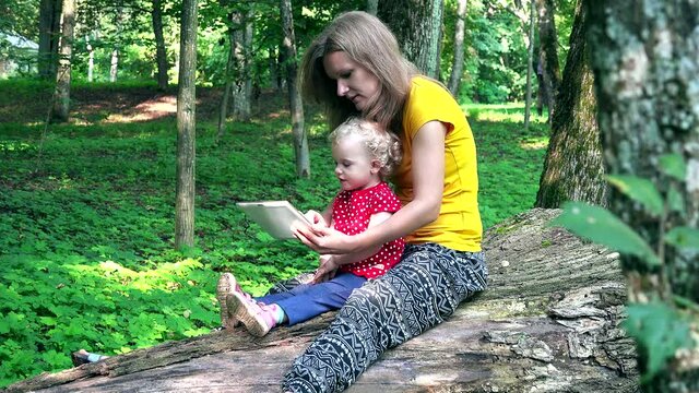 mother spend free time with little daughter playing tablet in green park. 4K
