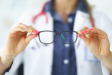 Woman in white medical coat holds glasses in her hands. Vision diagnostics by an optometrist concept