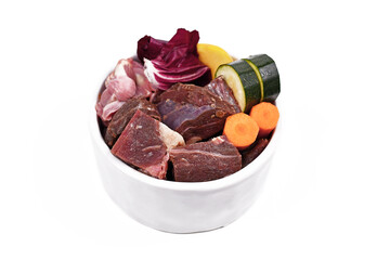 Dog bowl with species appropriated raw food like chunks of raw meat, chicken stomache and vegetabls like carrots, lettuce and zucchini isolated on white background