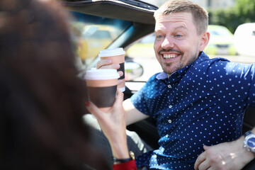 Man and woman are sitting in car and drinking coffee. Friendly meeting concept