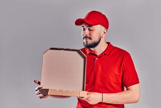 Delivery man in red cap, t-shirt giving food order pizza boxes isolated on gray background. Male employee pizzaman courier holding pizza in empty blank cardboard flatbox copy space. Service concept