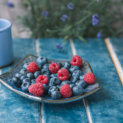 Food background. Ethno plate with blueberries, raspberries. Lavender on a blue background.