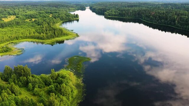 Aerial view of an elongated lake with winding coast and reflection of blue sky and clouds in water in the woods of Valday, Russia