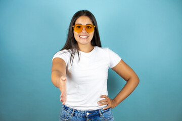 Young beautiful  woman wearing sunglasses smiling friendly offering handshake as greeting and welcoming