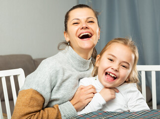 Young mother laughing and tickle her small daughter at sofa at home