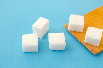Sugar cubes lie on a wooden spoon and a blue background, copy space