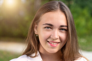 Portrait of a young girl outdoors on a summer evening. Sincere smile. Beautiful smiling teenage girl in a blue blouse, against a green summer park.