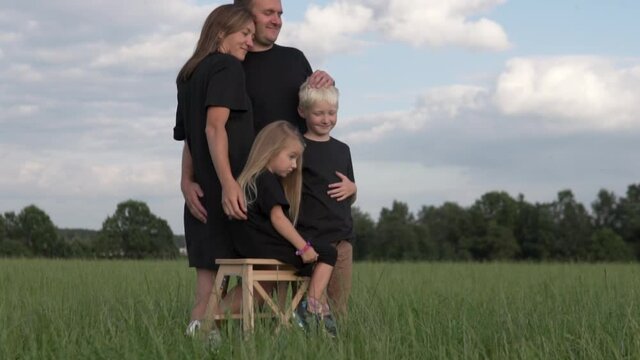 Family with children pose for a Photographer in a photo session in a field. Stylish family in black stands in a green field
