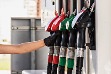 A woman's gloved hand reaches for a gasoline pump pistol at a gas station. Refueling the car