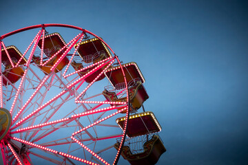 Red Ferris wheel at dusk, on indigo blue sky, illuminated. Carnival or circus retro background with...