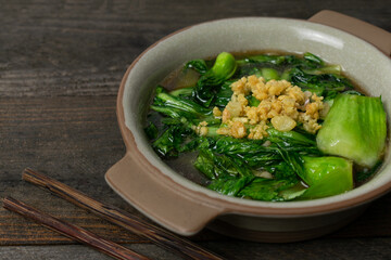 Fried Bok choy in oyster sauce with fried garlic in bowl on wooden table.