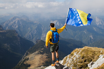 Man holding Bosnia and Herzegovina flag at the top of mountain