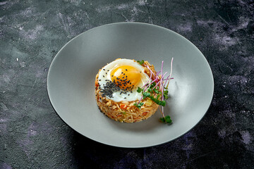 Rice fried in a wok with chicken and fried eggs in a gray plate on a black background. Asian street food