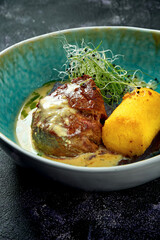 Grilled fillet mignon with mushroom sauce and polenta in a blue bowl on a black background